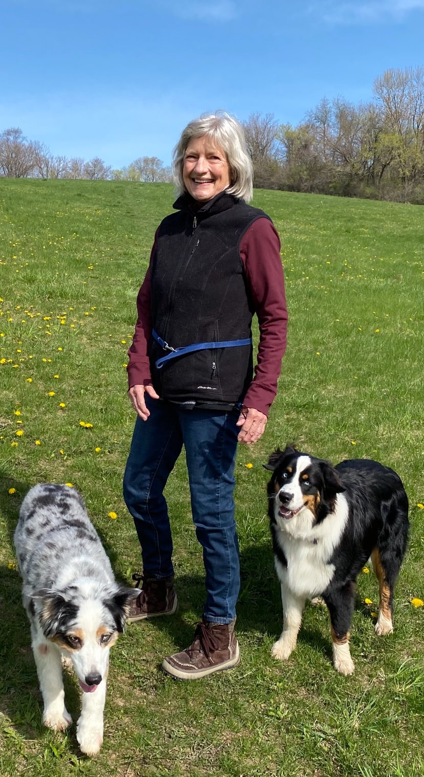 Photo of Sally Darley in a field with her two austrailian shepherd dogs.