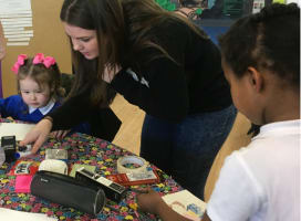 Two children at a table doing art with adult helping