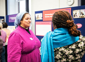Two people in colourful clothing talking in front of a display board