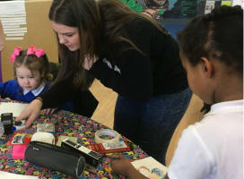 Two children at a table doing art with adult helping