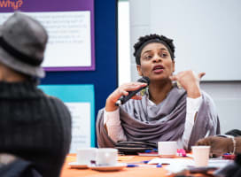 A black female-presenting speaker holding a microphone and talking to people off camera