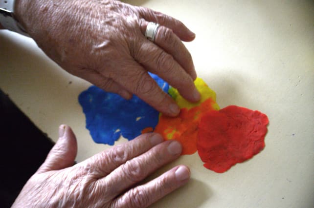 Image of two hands squashing red, orange, yellow and blue playdough.