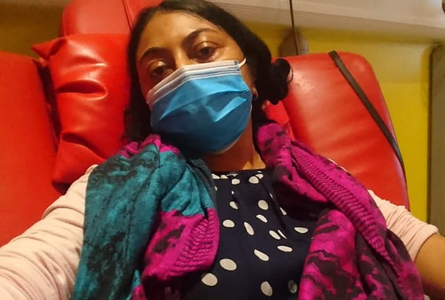 Person looking into camera whilst sitting on a sofa chair receiving drip treatment
