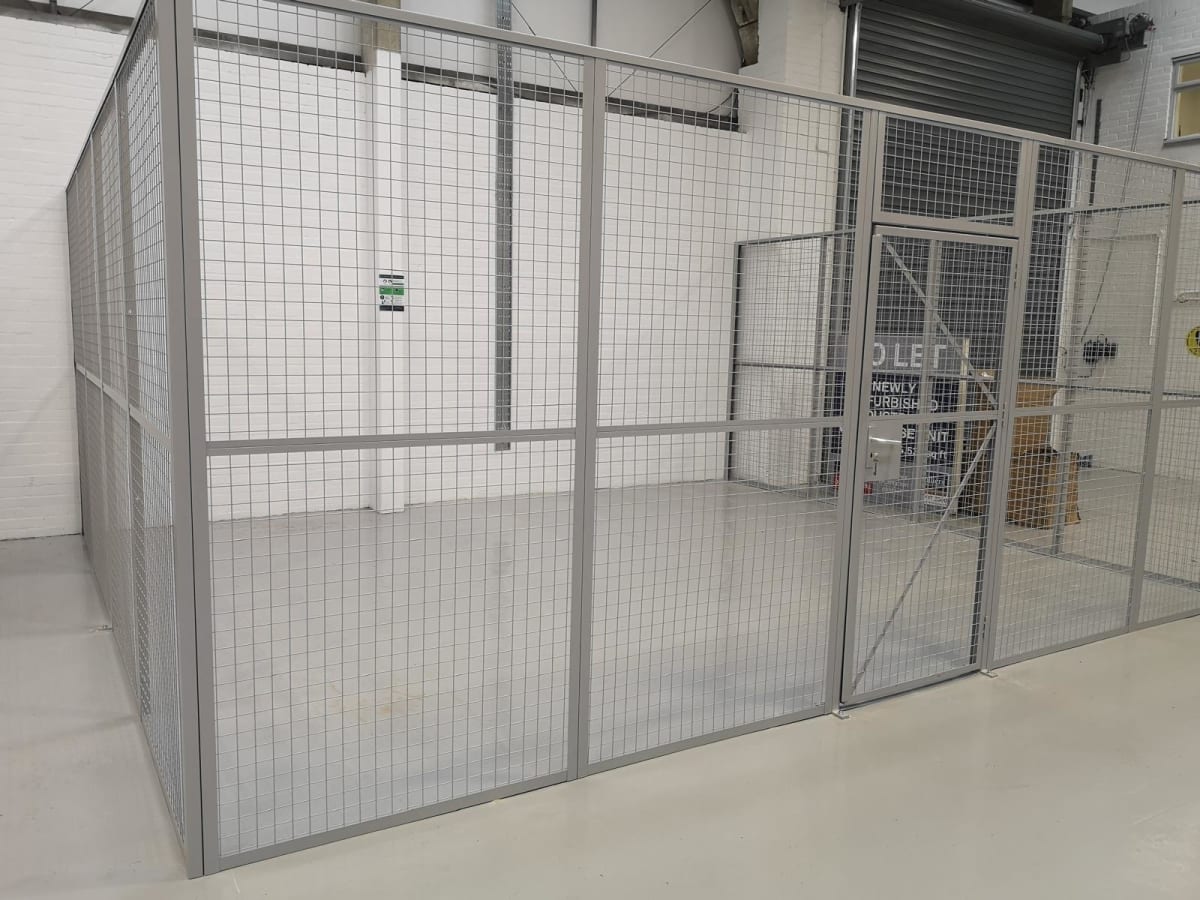 Light grey mesh security cage with a single door installed on a warehouse floor