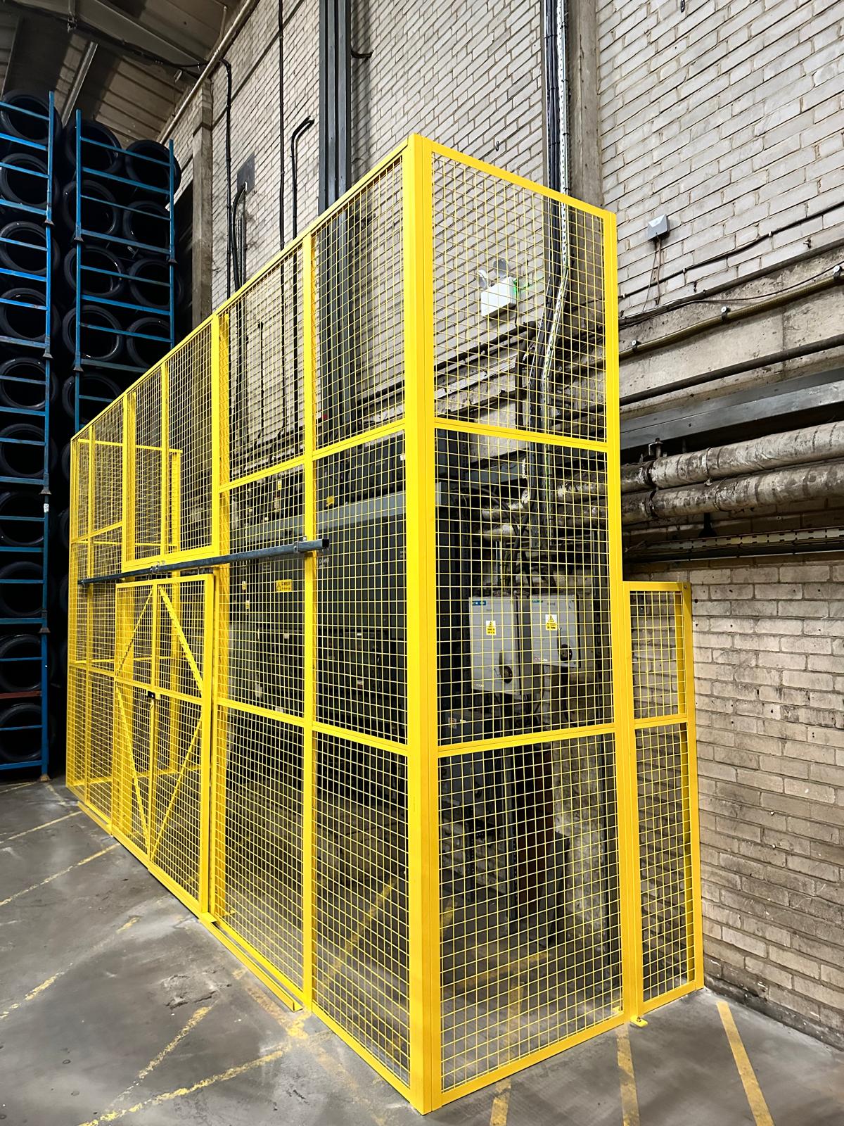 Yellow mesh security cage built around electrical cabinets and pipework on a factory floor