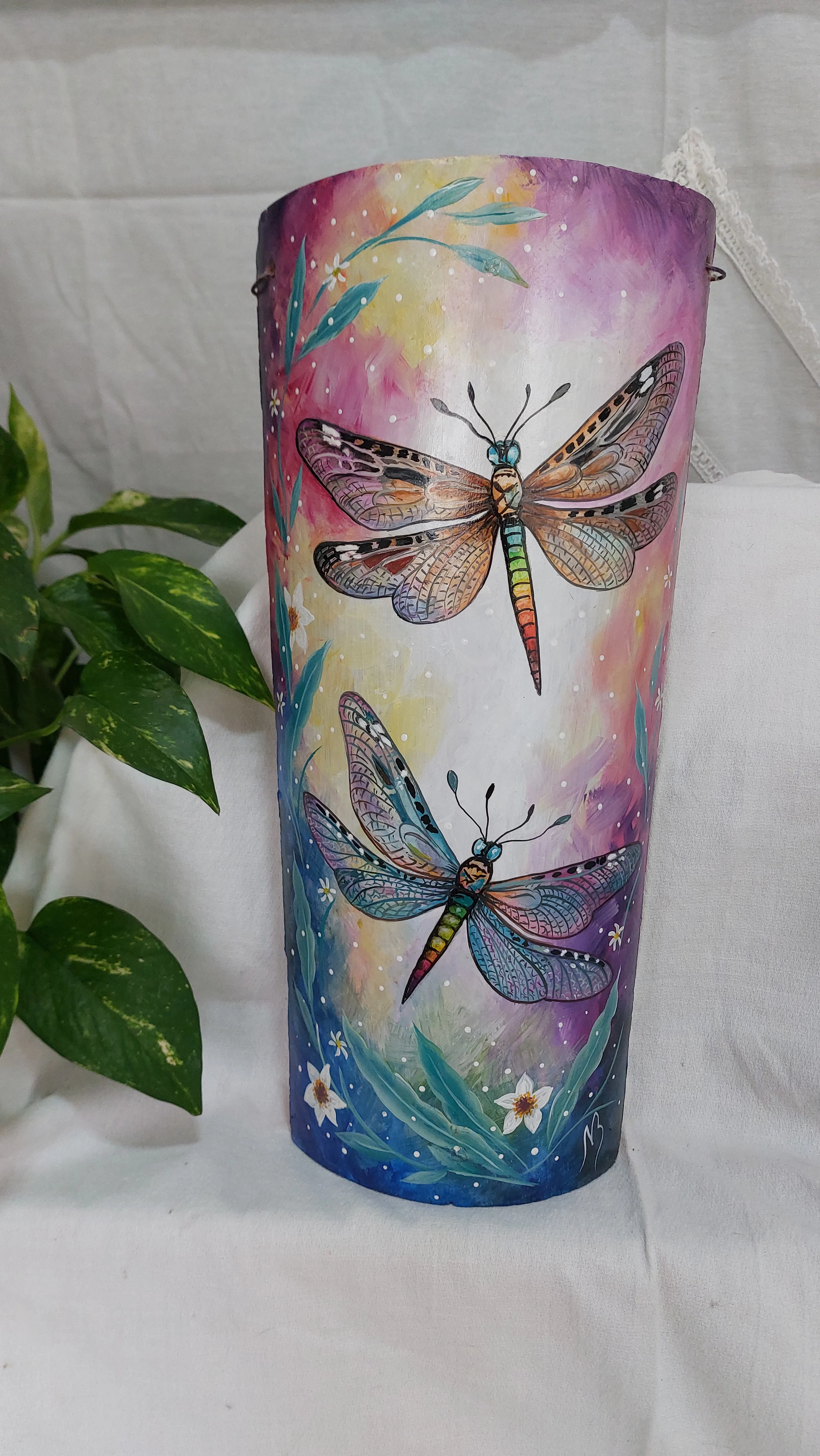Teja colonial pintada a mano, con dos libélulas decorativas de colores vibrantes, detalles de patrones en las alas y un fondo artístico difuminado en tonos pastel y violeta con pequeñas flores silvestres.