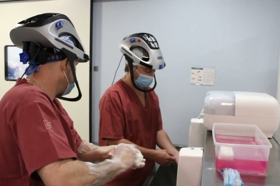 Dos cirujanos con traje y casco quirúrgico se lavan las manos antes de una cirugía