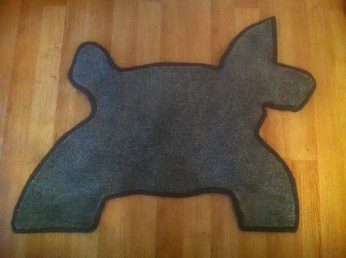 Dog-shaped grey carpet rug with black whipped edging, displayed on a wooden floor