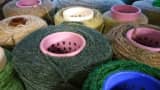 Close-up of several spools of natural yarn in green, tan, and brown shades, with colourful plastic centers, used for professional carpet whipping.
