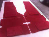 Set of red, custom-shaped car carpets with matching whipped edging, laid out for display.