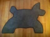 Dog-shaped grey carpet rug with black whipped edging, displayed on a wooden floor.