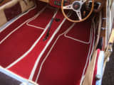 Red carpet set with cream whipped edging, perfectly fitted in a classic car interior with wooden steering wheel and trim.