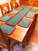 Dining table set with green carpet mats and a matching runner, all finished with red whipped edging.