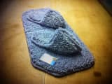 Pair of slippers made from grey carpet remnants, displayed on a matching whipped mat.