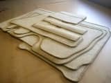 Stack of custom-shaped, beige carpet templates for a vehicle, each with whipped edging.