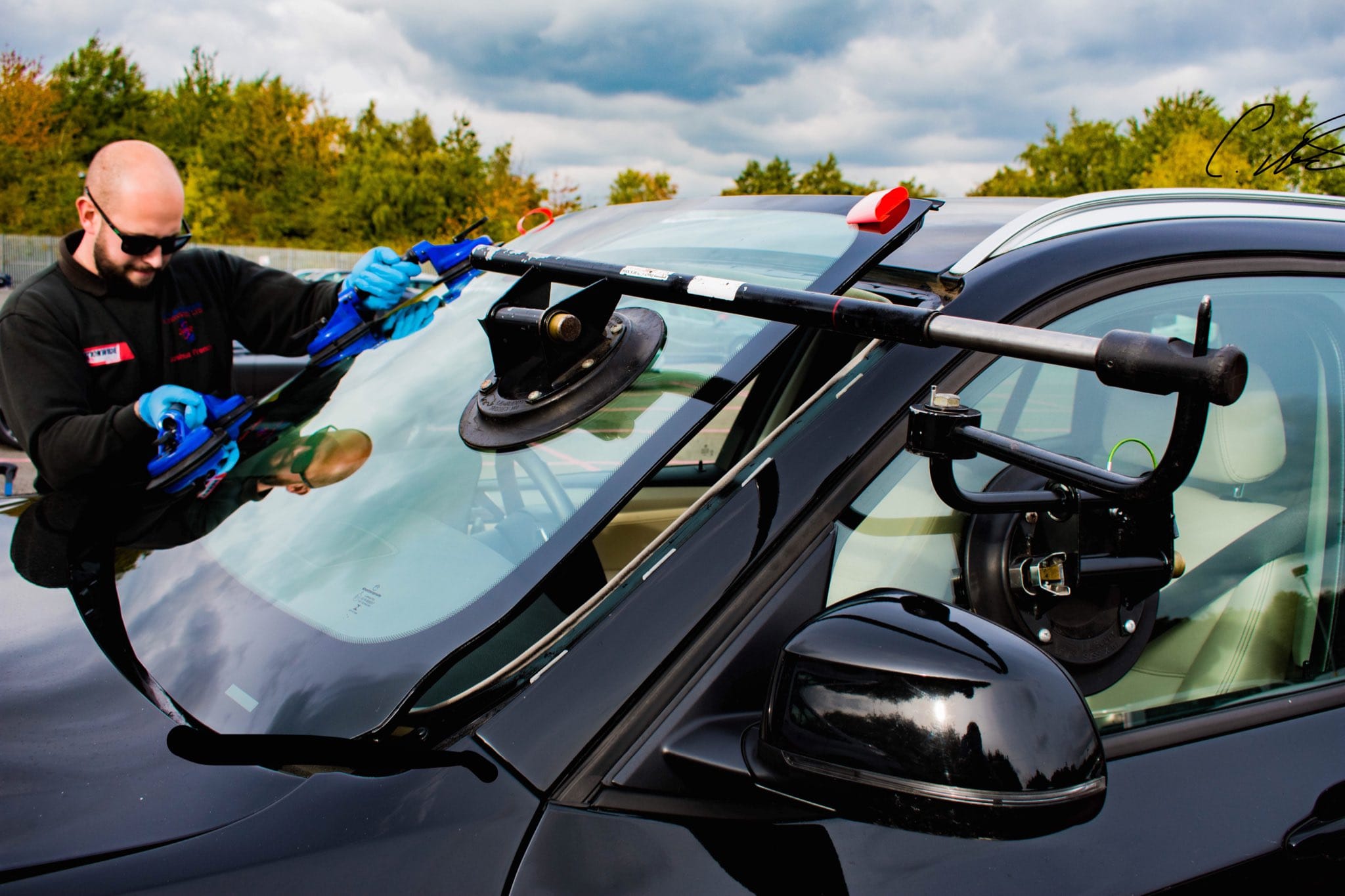 An auto glass technician uses professional tools to replace the windshield on a black car