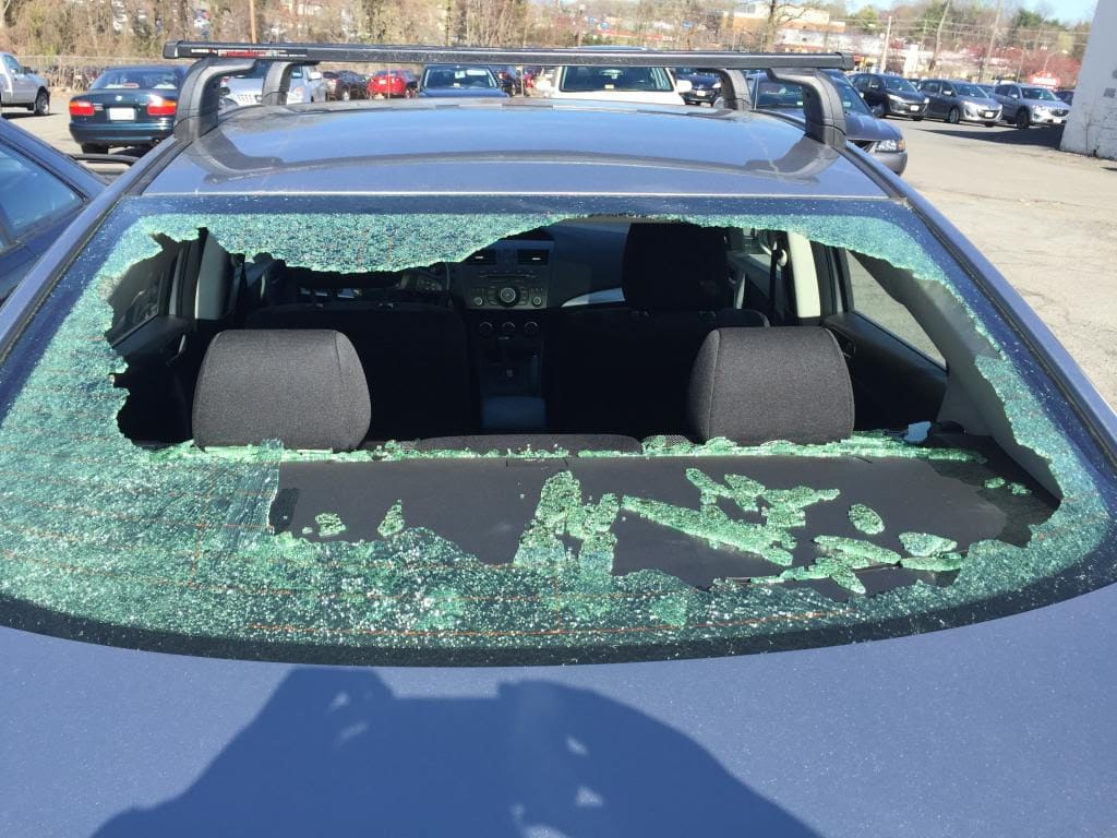 A car with a severely shattered rear window, highlighting the need for back glass replacement.