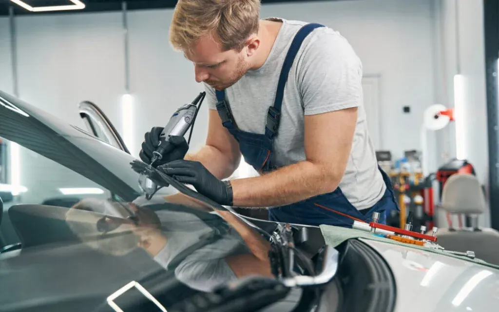 Car service technician checks crack on car windshield closeup. Man in workshop