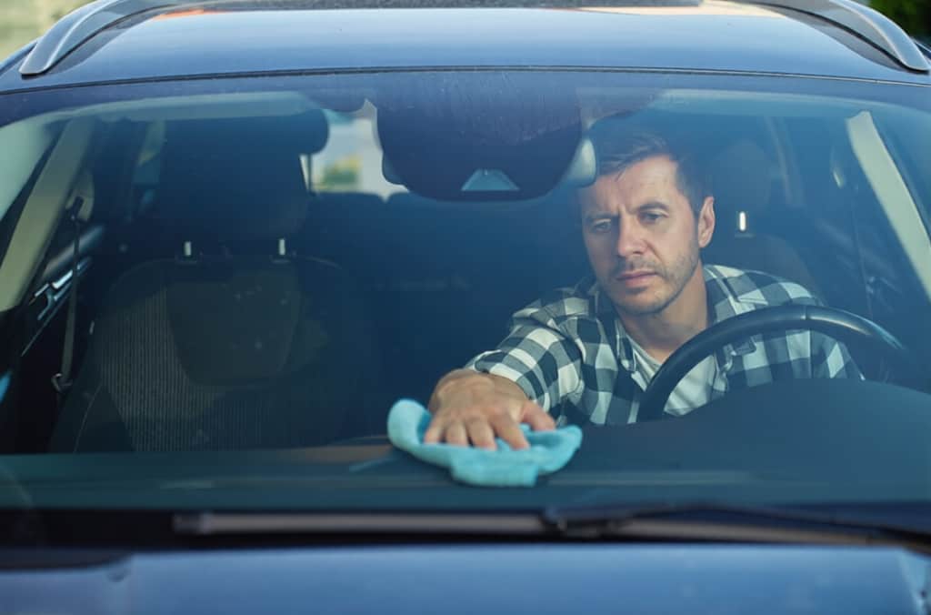 Man cleaning car dashboard from inside of car