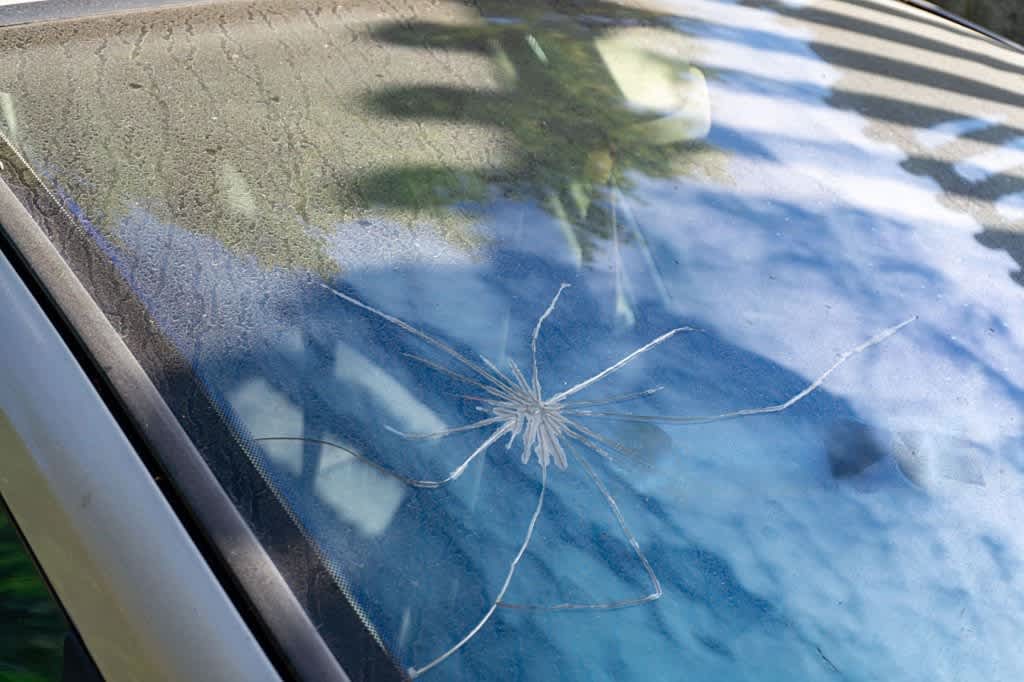 Cracked car windshield with radial damage, visible dust on glass, light reflections and tree reflections
