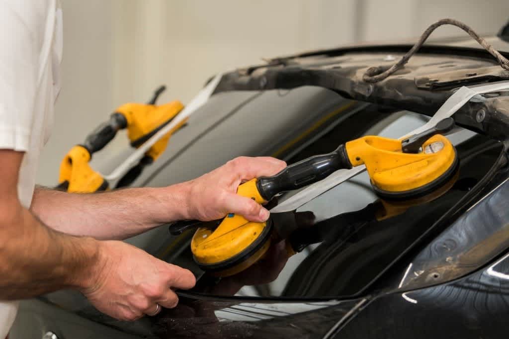 Side view of a rear car window with equipment with suction cops used during replacement of a broken car window. Hands of a car mechanic is visible