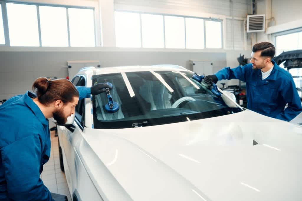 A professional mechanic changes a windshield on a car in a car workshop. Hands mechanic holding a tool. Replacement of automobile glasses.