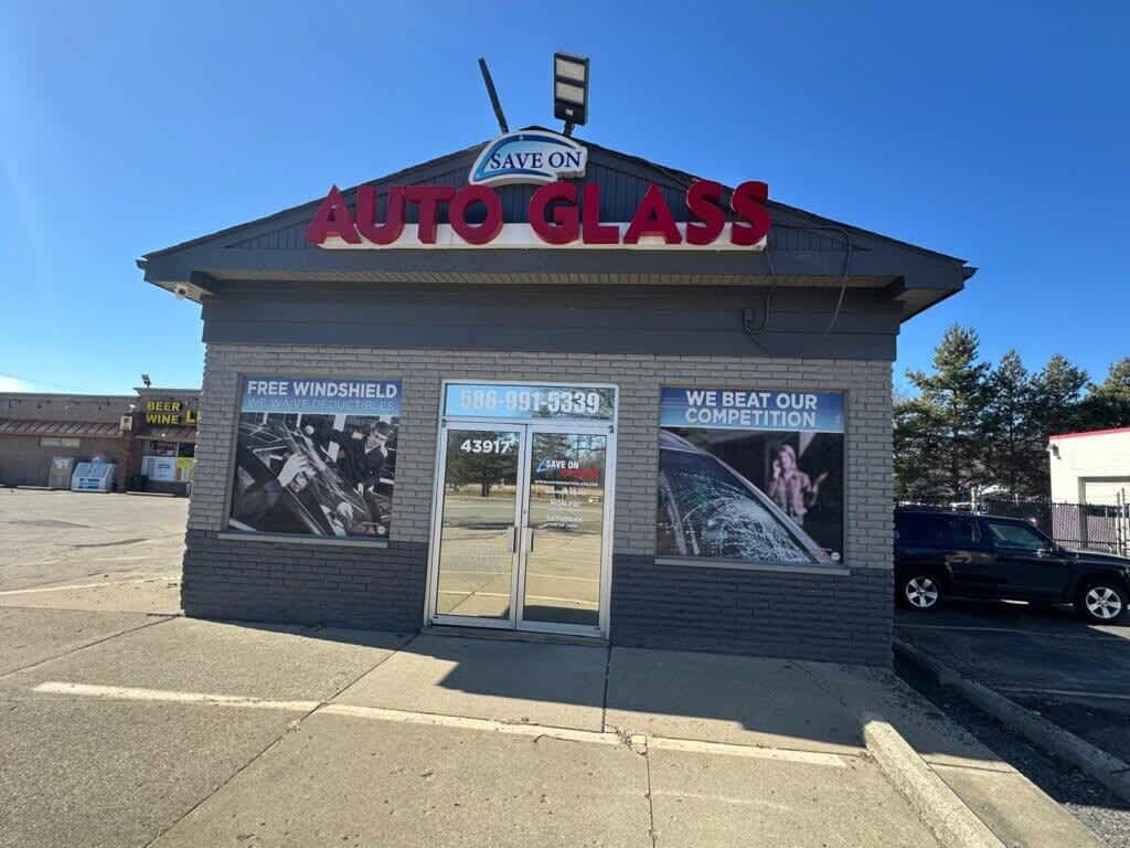 Exterior view of the Save On Auto Glass shop located at 43917 Van Dyke Ave, Sterling Heights, MI, displaying promotional signs for free windshield replacement and competitive pricing.