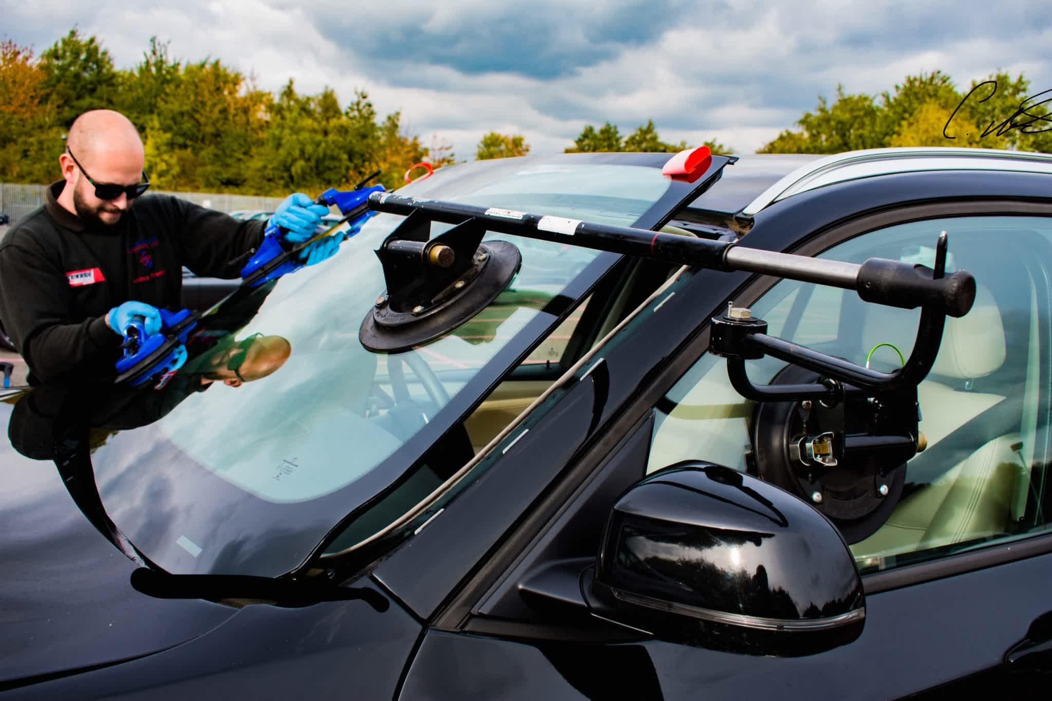 An auto glass technician uses professional tools to replace the windshield on a black car