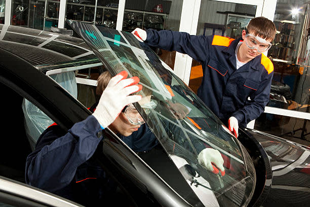 Two Real Mechanics changing the broken windshield of black car in an auto repair shop