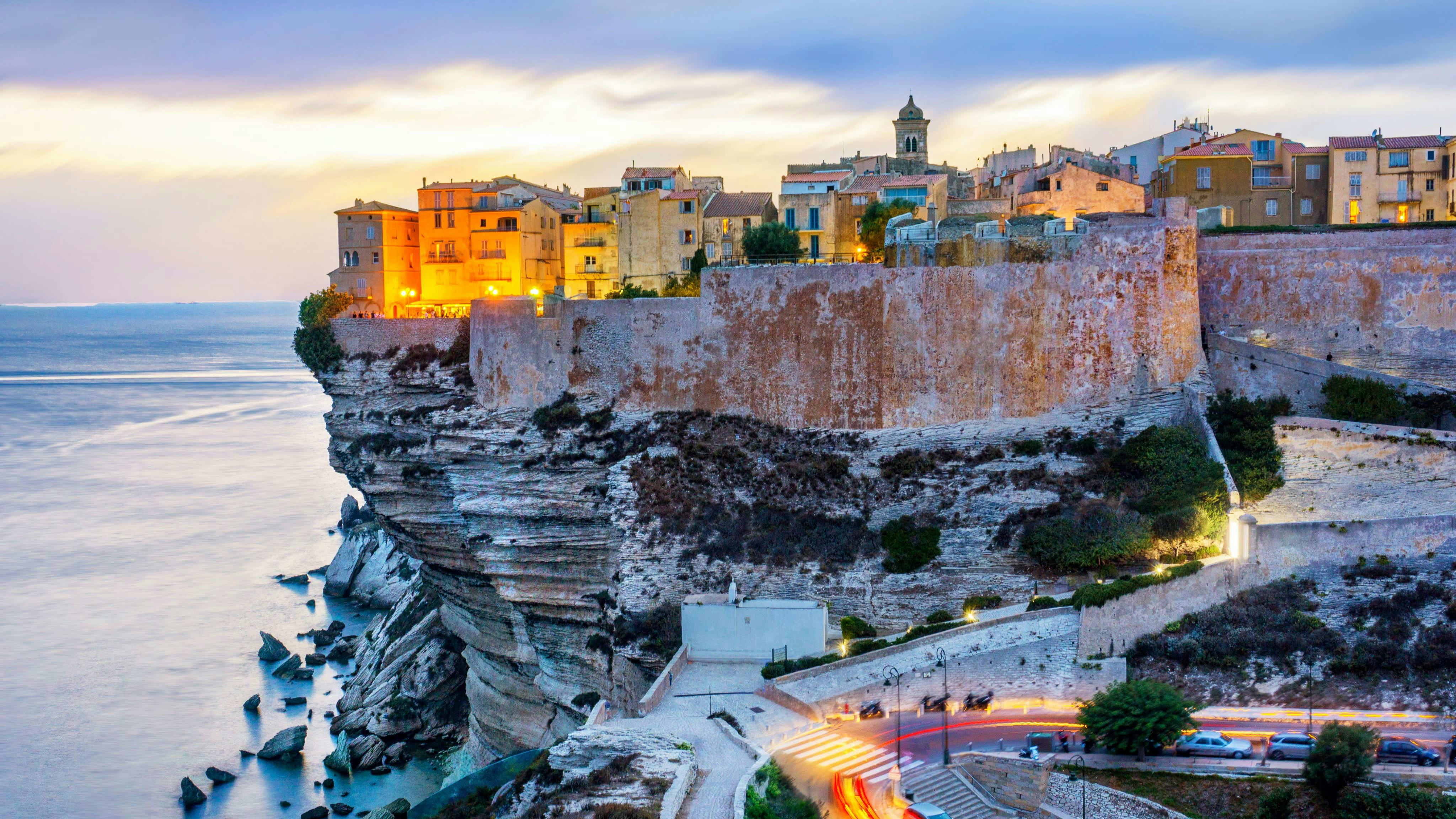 Illuminated clifftop citadel of Bonifacio reflected in the calm Mediterranean Sea at dusk, southern Corsica France