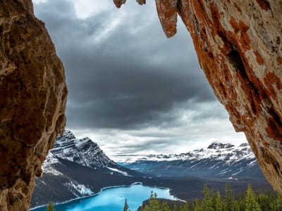 Vivid turquoise Peyto Lake seen through a natural rock arch with snow-capped Rocky Mountains in Banff National Park, Canada
