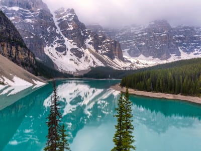Turquoise glacial lake surrounded by pine trees and snow-capped mountains