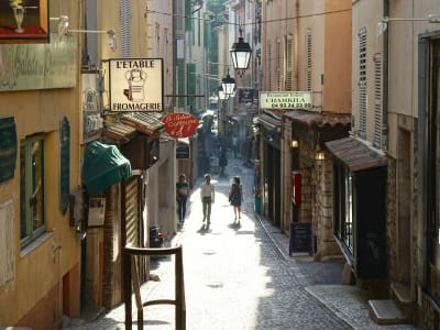 Charming narrow street in Antibes old town with yellow facades, lanterns and pedestrians on the French Riviera