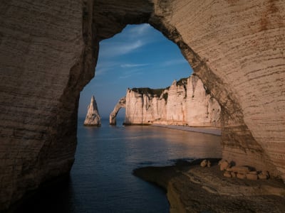 View through a natural sea cave arch at Étretat looking out to the Normandy coastline at dusk, France
