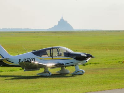Small light aircraft on a grass airfield with Mont-Saint-Michel visible on the horizon, Normandy France