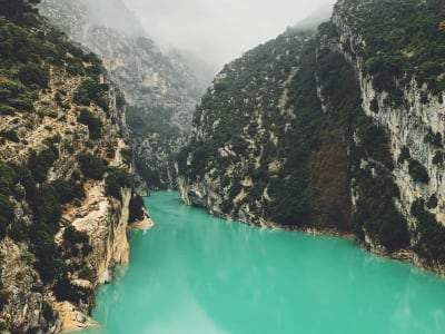 Looking down into the misty Gorges du Verdon gorge with turquoise water between towering limestone walls, France