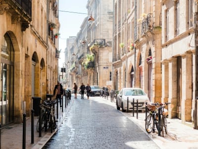 Busy pedestrian street in central Bordeaux with classic stone facades, cyclists and wet cobblestones, France