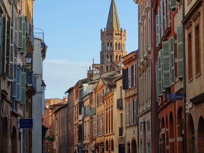 Narrow Rue du Taur in Toulouse with the distinctive pink brick bell tower of the Notre-Dame du Taur church, France
