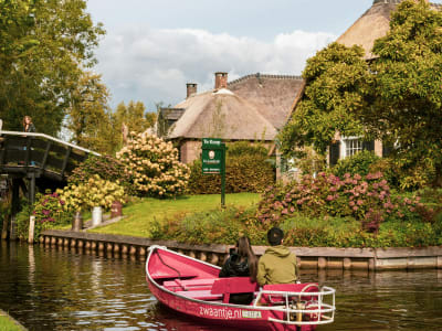 Wooden footbridge over a canal with manicured gardens and a thatched cottage in Giethoorn, Netherlands