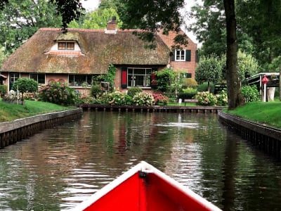 Red canoe on a quiet canal with a thatched-roof cottage and lush garden in Giethoorn, Netherlands