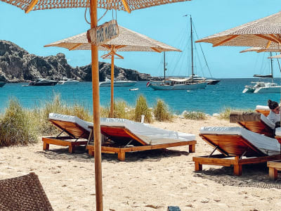 Beach loungers with straw umbrellas and sailboats in a sheltered bay Mallorca Spain