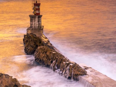 Lighthouse on rocky promontory at dramatic sunset in San Sebastián Basque Country Spain