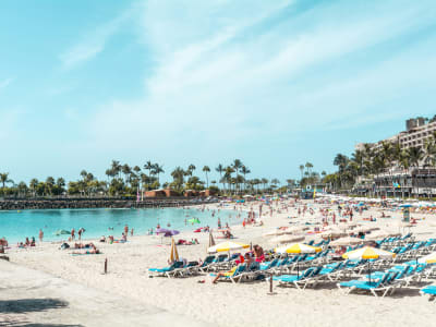 Busy Playa de las Américas beach Tenerife with sunbathers colorful parasols and hotels Canary Islands
