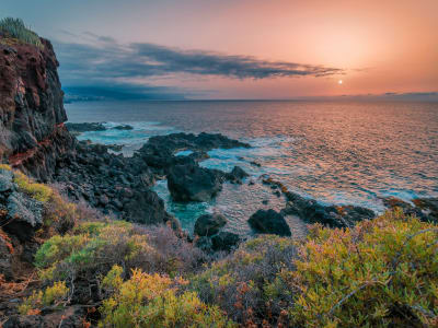 Rocky Tenerife coastline at sunset with orange sky and calm turquoise sea Canary Islands Spain
