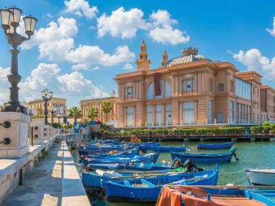 Ornate historic theatre building with blue fishing boats moored in the harbour of Bari, Italy