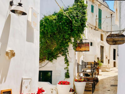 Charming whitewashed alley with green ivy, terracotta pots and restaurant sign in Ostuni old town