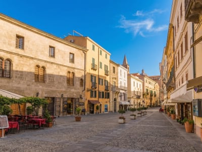 Sunny cobblestone street with cafe terraces and historic stone buildings in Alghero old town, Sardinia