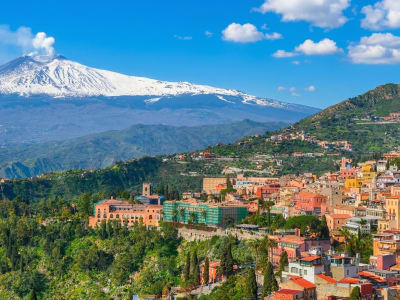 Mount Etna with snow on its summit towering above the colourful hilltop town of Taormina, Sicily