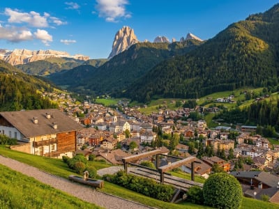 Tyrolean village with traditional houses on a green hillside surrounded by Dolomite peaks in Val Gardena