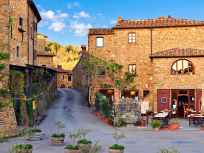 Medieval stone village square with terracotta pots and a restaurant terrace in the Chianti region, Tuscany